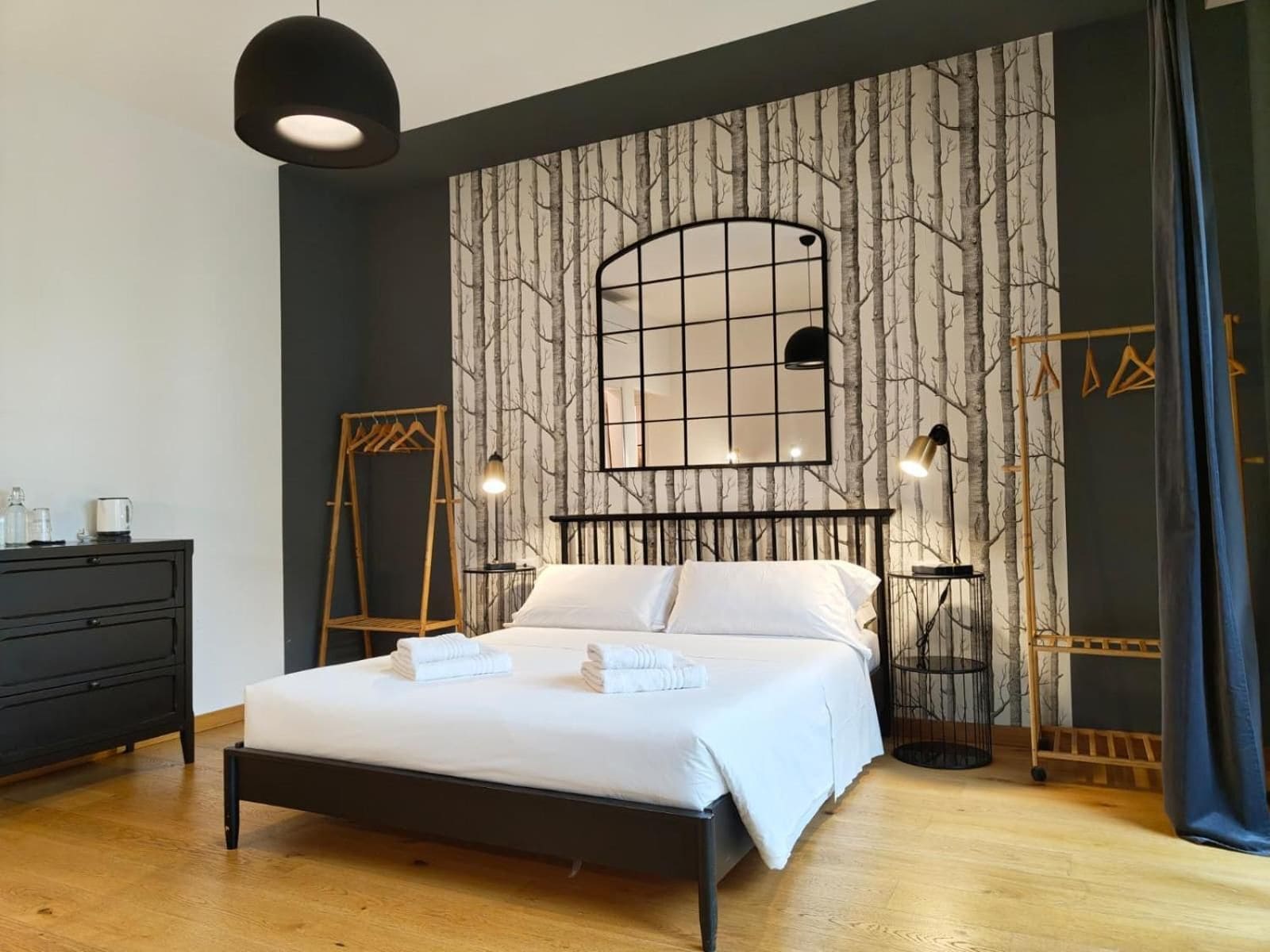 Un dormitorio con cama, cómoda, lámpara colgante y pared decorada con un diseño de árbol.