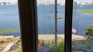 Uitzicht door een raam op een meer met bootjes, een gazon en huizen op de achtergrond.
