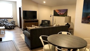 A living room with a sofa, a TV, a dining table with chairs, and artwork on the walls.
