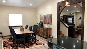 A dining area with a wooden table and chairs, a kitchen island, and a large mirror.