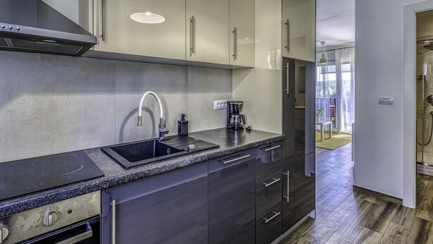 Une cuisine moderne avec des meubles de couleur sombre, une hotte de cuisinière en acier inoxydable, un évier doté d’un robinet incurvé et une machine à café posée sur le plan de travail.