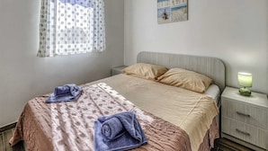 Une chambre à coucher avec un lit, des oreillers, une table de chevet avec une lampe, une fenêtre avec des rideaux et un tableau au mur.