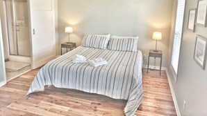 A bedroom with a bed, two bedside tables, a standing fan, and a door leading to a shower. - Secluded 3BR private home on golf course! (Edisto Beach)