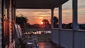 A wooden porch with a railing, a view of the sunset over water, and a lamp post. - Secluded 3BR private home on golf course! (Edisto Beach)