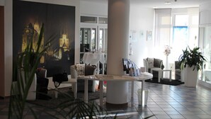 Un moderno vestíbulo de hotel con un cuadro grande de un paisaje urbano, una mesa redonda blanca y cómodas zonas de estar.