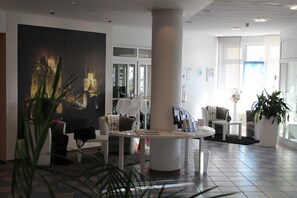 Un moderno vestíbulo de hotel con un cuadro grande de un paisaje urbano, una mesa redonda blanca y cómodas zonas de estar.