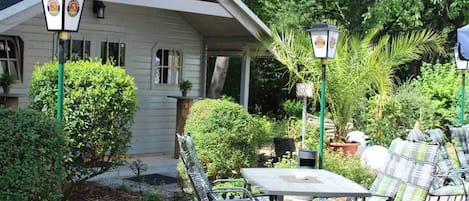 A patio area with a table and chairs, surrounded by greenery and a house.