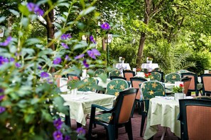 Un área de comedor al aire libre con mesas y sillas, rodeada de abundante vegetación y árboles.