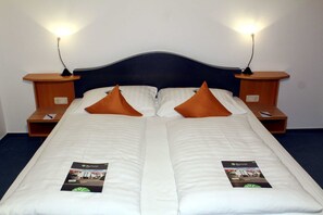 Una cama doble con dos almohadas, mesitas de noche y un folleto a cada lado.
