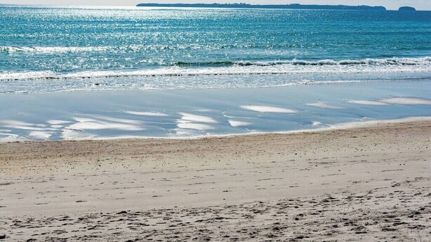 Ein Strand mit klarem, blauem Wasser und sandigem Ufer.