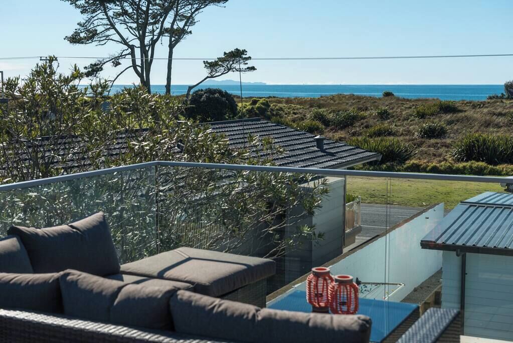 A balcony with a sofa and a glass railing overlooking a coastal landscape.
