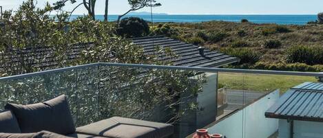 A balcony with a sofa and a glass railing overlooking a coastal landscape.