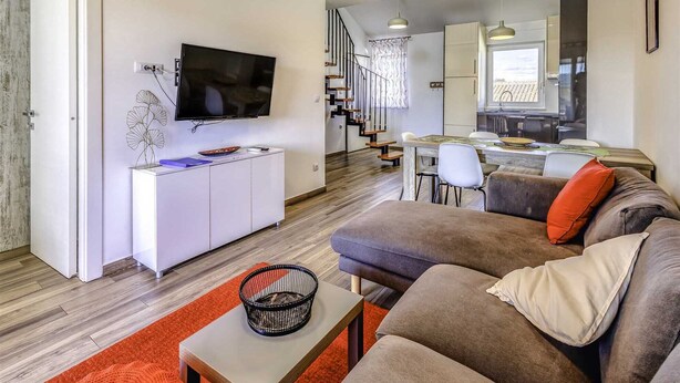 Een moderne woonkamer met een flatscreen televisie, een bank, een salontafel en een eethoek met een tafel en stoelen.