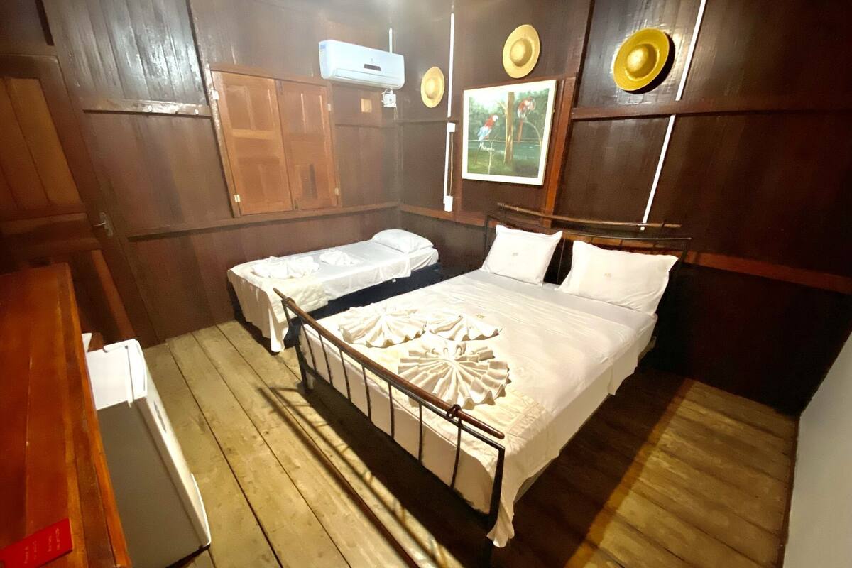Ein Zimmer mit zwei Betten, Holzboden, einem Holzschrank und einer Wand-Klimaanlage.