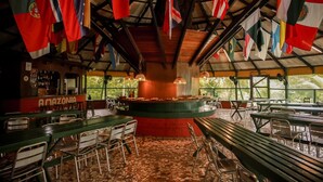 Ein Restaurant mit einer zentralen Bar, mehreren Esstischen und Stühlen. An der Decke hängen Flaggen verschiedener Länder.