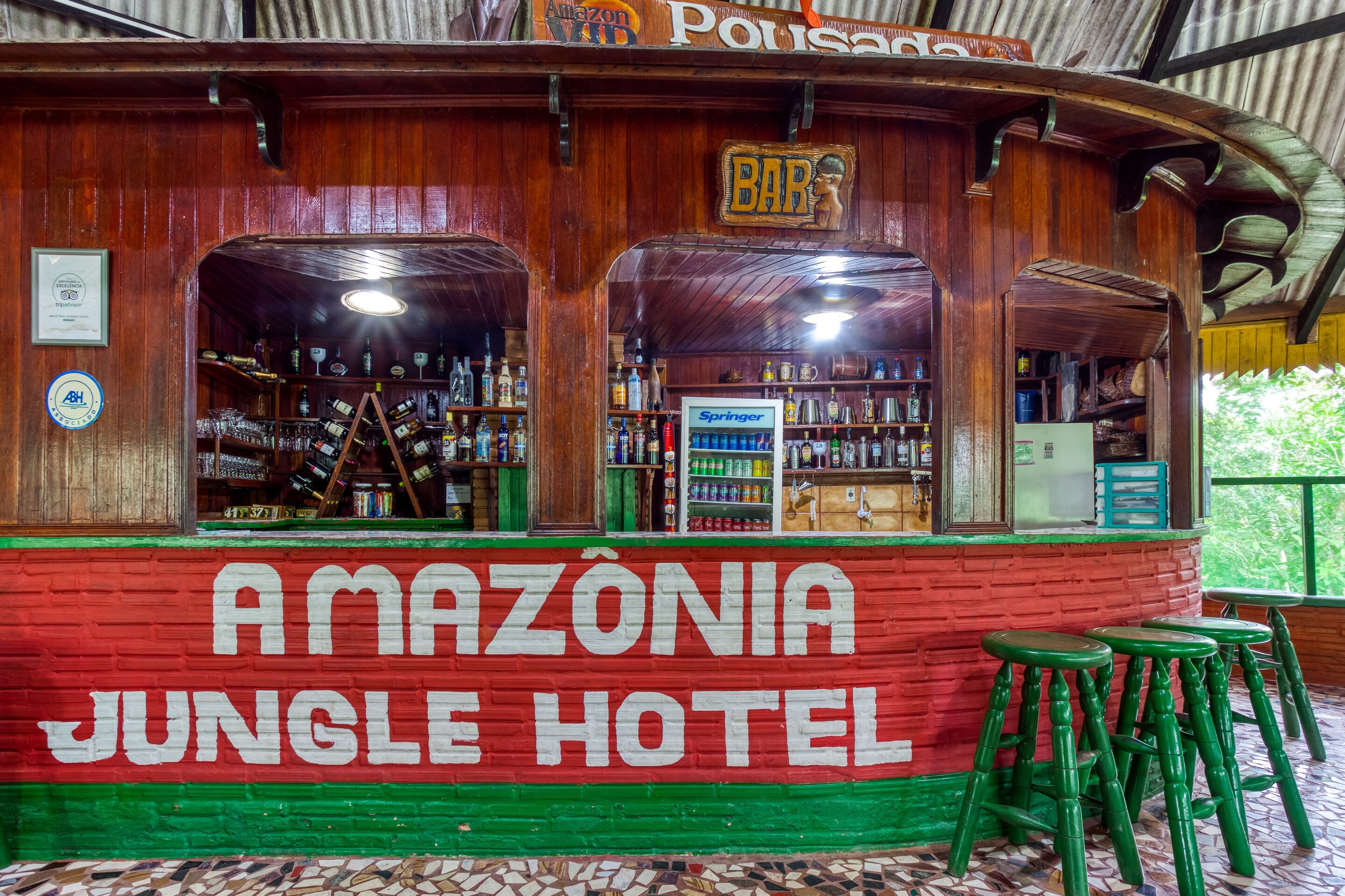 A wooden bar area with a sign reading "AMAZÔNIA JUNGLE HOTEL" and a "BAR" sign above it.