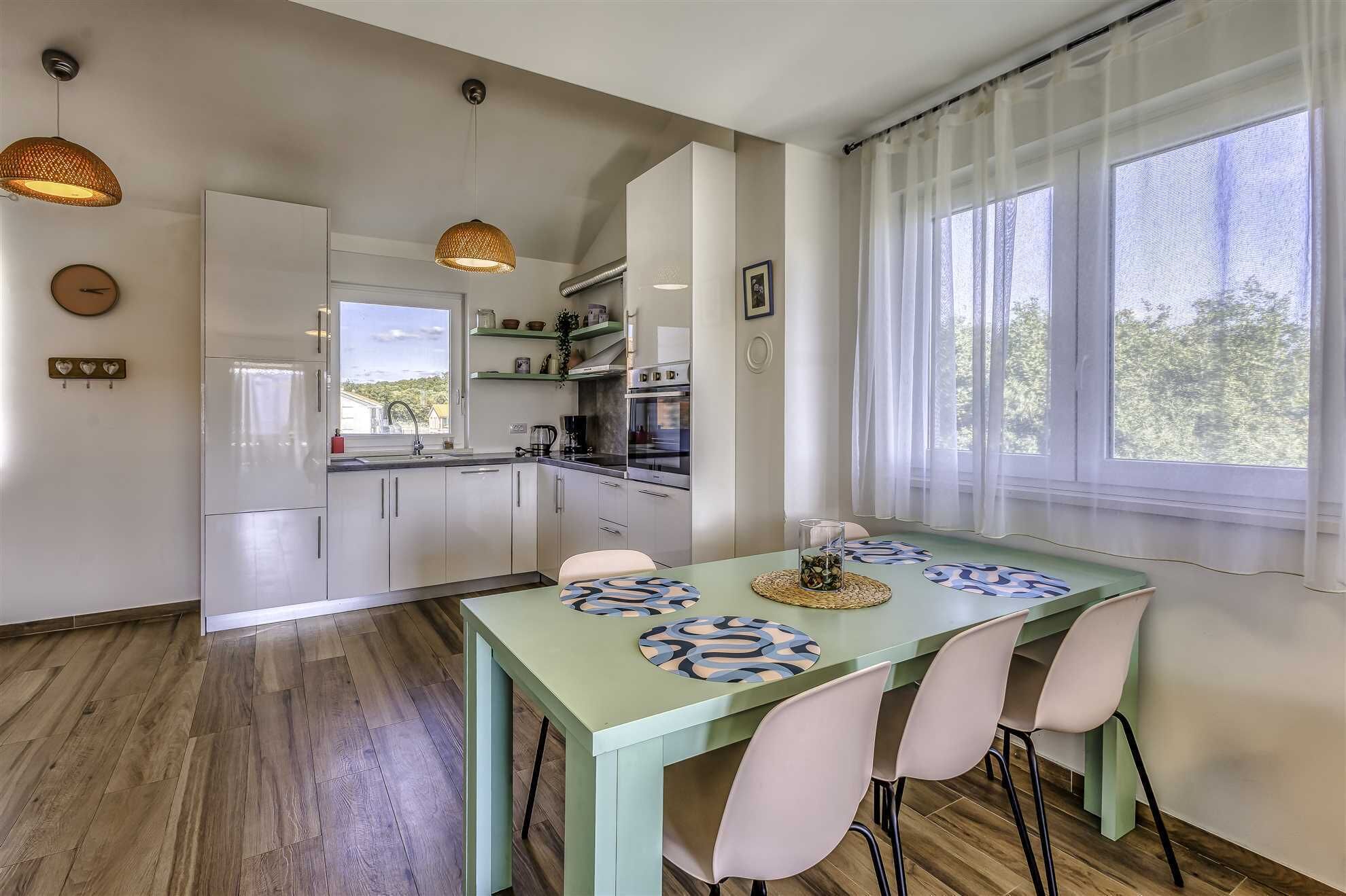 A modern kitchen with white cabinets, a built-in oven, and a window overlooking greenery.