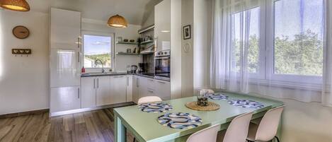 A modern kitchen with white cabinets, a built-in oven, and a window overlooking greenery.