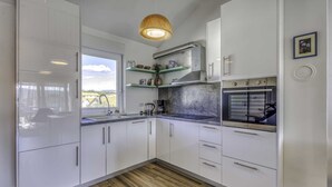 Ett modernt kök med vita skåp, en inbyggd ugn och ett fönster med utsikt över hus.