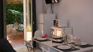 Un coin repas avec une table dressée pour deux personnes, un téléviseur fixé au mur et une chaise verte à l’extérieur.