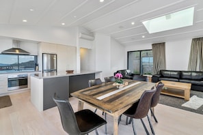 A modern kitchen with a central island, a dining area with a wooden table, and a living room with a black leather sofa.