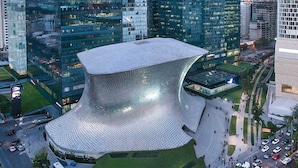 A modern building with a unique, curved glass facade and a distinctive, dome-like structure at the center. - Polanco Super Lujo (Mexico City)