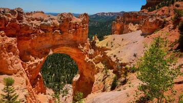 Formación natural de arco de roca rodeada de colinas boscosas.