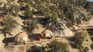 Un hébergement de type yourte doté d’une terrasse en bois et d’un espace clos, situé dans un cadre montagneux.