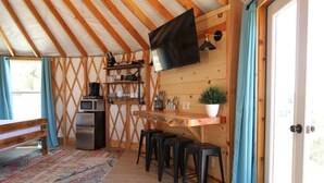 Une pièce chaleureuse avec un plafond en bois, un téléviseur fixé au mur, un coin cuisine équipé d’un four à micro-ondes et un espace détente avec des tabourets.