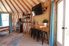 Tunnelmallinen huone, jossa on puinen katto, seinälle asennettu televisio, mikroaaltouunilla varustettu keittiö sekä oleskelualue, jossa on jakkaroita.