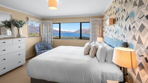 Een slaapkamer met een groot bed, een dressoir, een stoel en uitzicht op bergen en een meer.