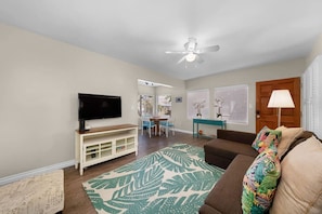 A living room with a television, a ceiling fan, a sofa, and a dining area with a table and chairs.