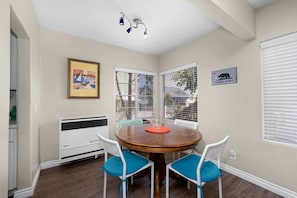 Un coin repas comprenant une table ronde, deux chaises, un luminaire au plafond et une fenêtre avec des stores.