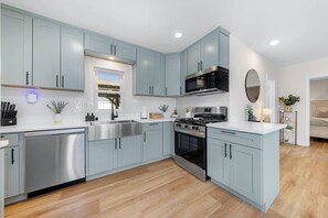 A modern kitchen with light blue cabinets, stainless steel appliances, and a wooden floor. - Suite Cozy Beach Nook, 150 Steps To The Sand (San Diego)