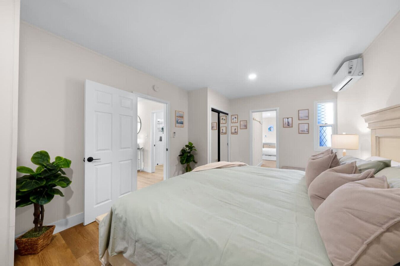 A bedroom with a bed, a potted plant, a door, and a wall-mounted air conditioner.