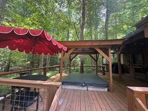 A wooden deck with a red canopy, a bench, and a view of a forest.