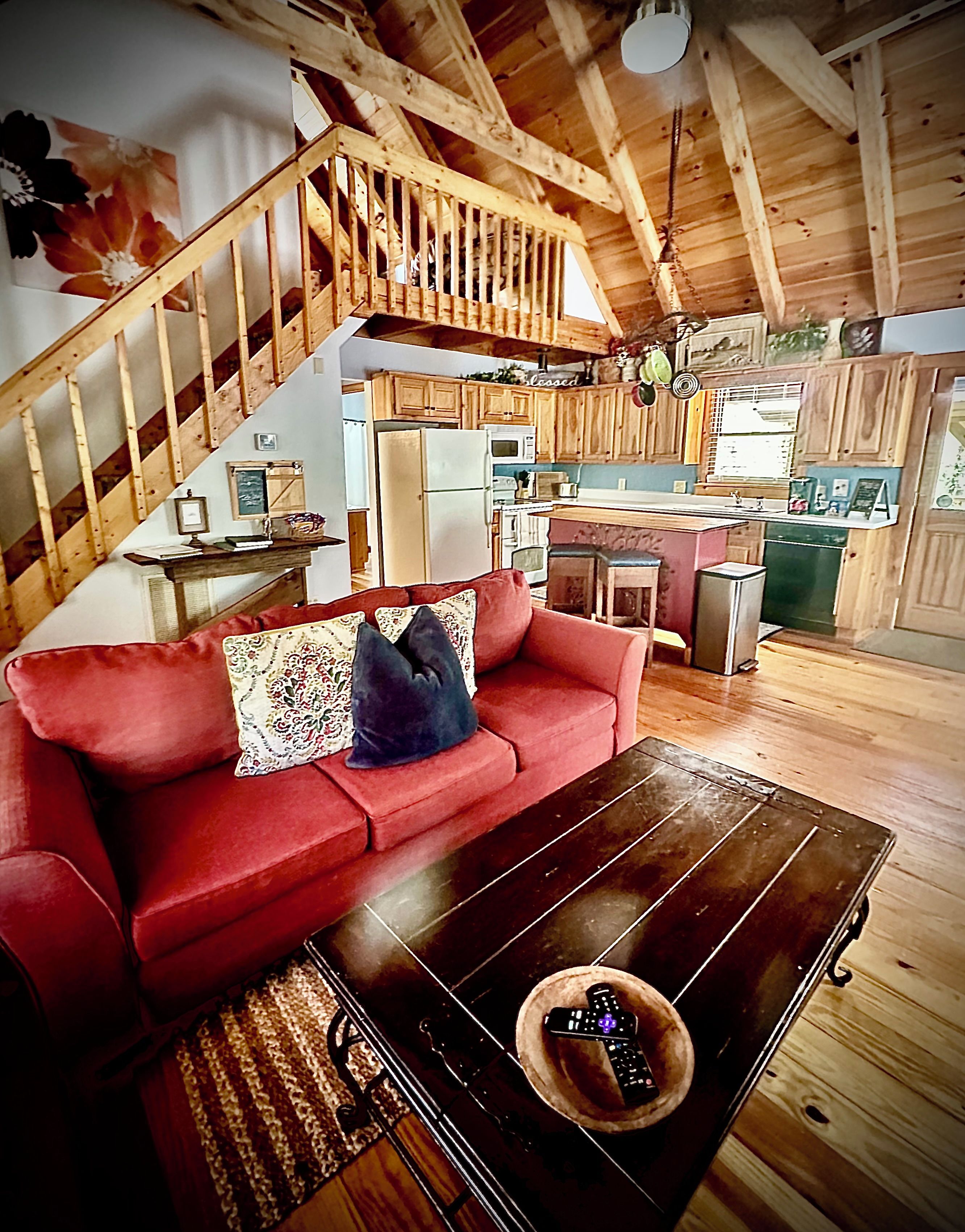 A wooden interior with a red sofa, a wooden coffee table, and a kitchen area with wooden cabinets and appliances.