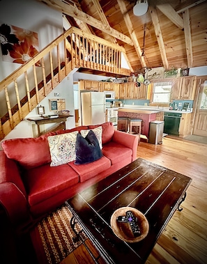 A wooden interior with a red sofa, a wooden coffee table, and a kitchen area with wooden cabinets and appliances.