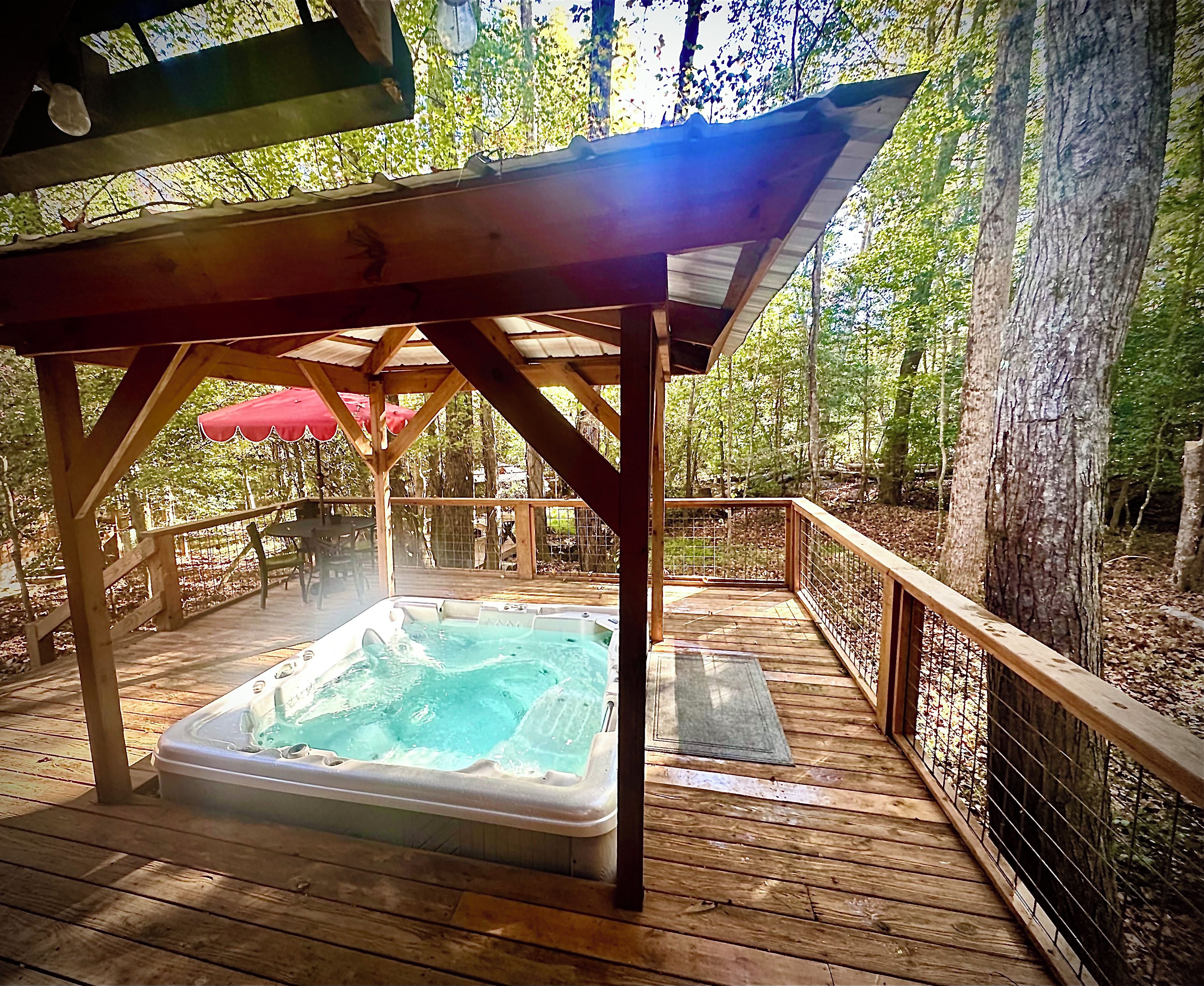 A wooden deck with a hot tub, surrounded by trees and a wooden fence.