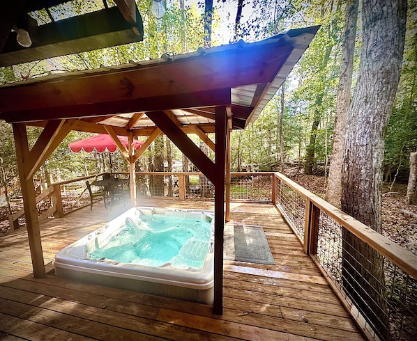 Una terraza de madera con jacuzzi, rodeada de árboles y una valla de madera.