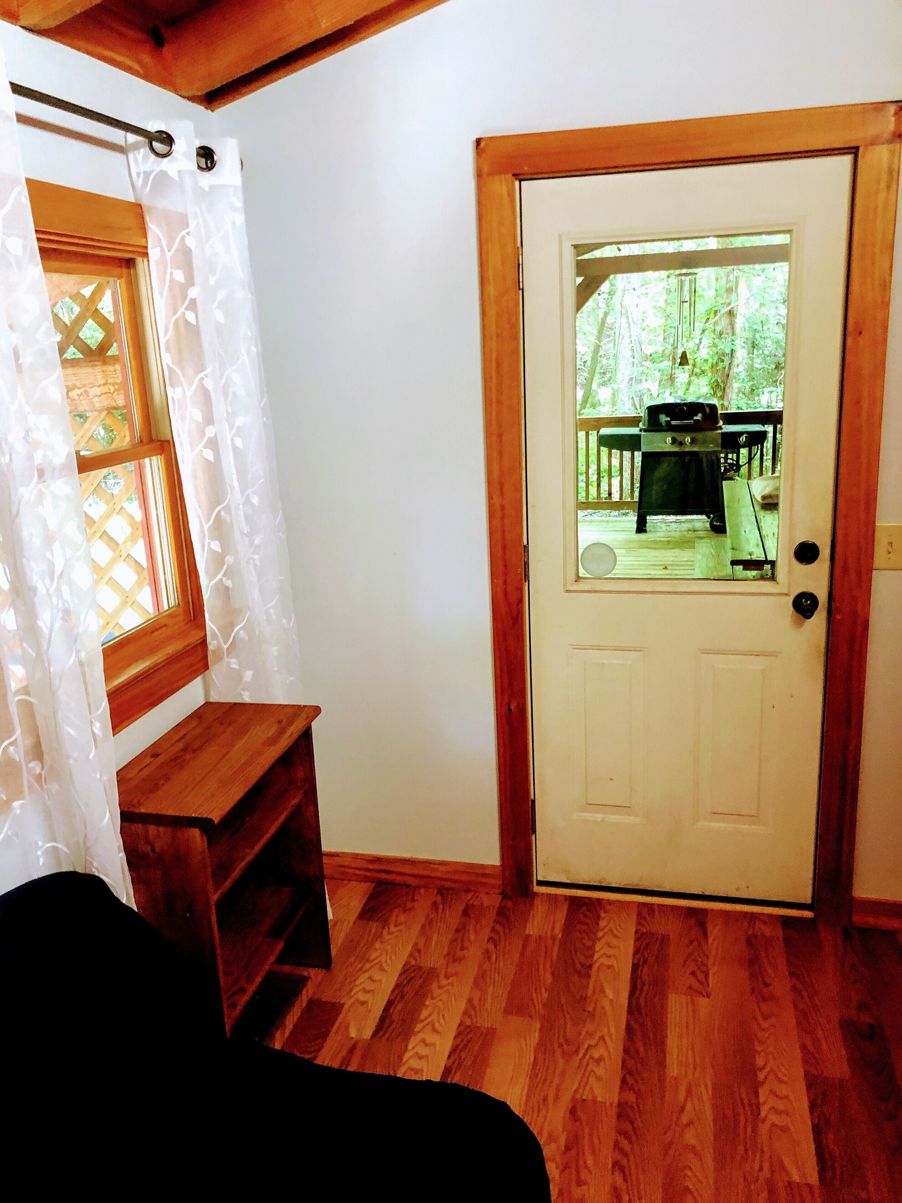 Een kamer met een houten bankje, een deur die naar buiten leidt, en uitzicht op een terras met tuinmeubilair.