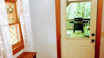 Een kamer met een houten bankje, een deur die naar buiten leidt, en uitzicht op een terras met tuinmeubilair.