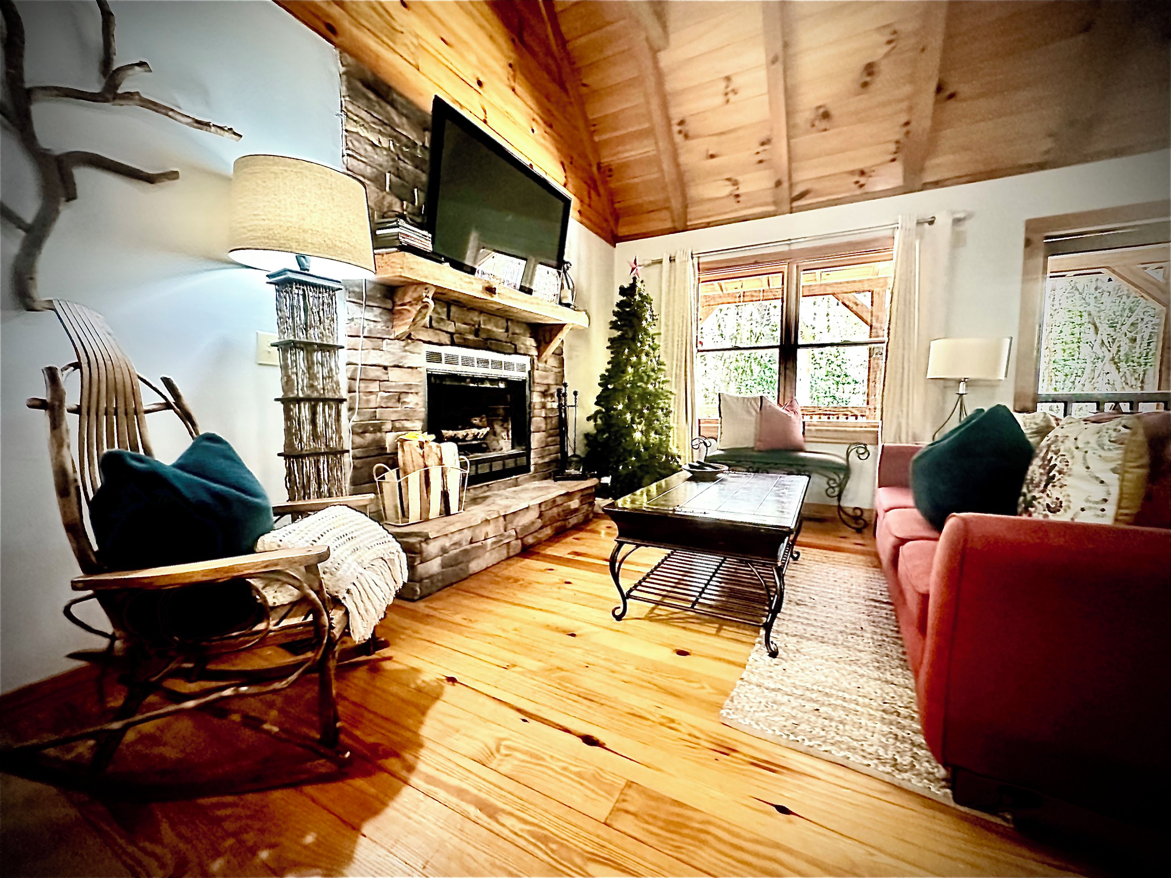 A cozy living room with a fireplace, a television mounted above it, a Christmas tree, and a red sofa.