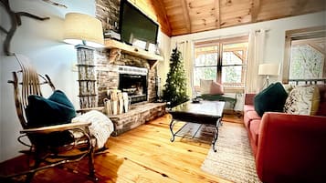 A cozy living room with a fireplace, a television mounted above it, a Christmas tree, and a red sofa.