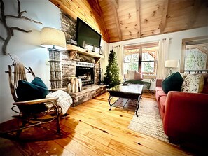A cozy living room with a fireplace, a television mounted above it, a Christmas tree, and a red sofa. - Majestic, private cabin with hot tub/multiple deck...a little taste of heaven! (Dahlonega)