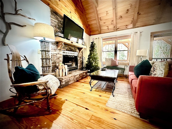 A cozy living room with a fireplace, a television mounted above it, a Christmas tree, and a red sofa.
