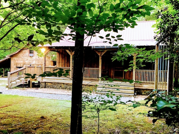 A rustic wooden cabin with a porch and a small staircase leading to a deck.