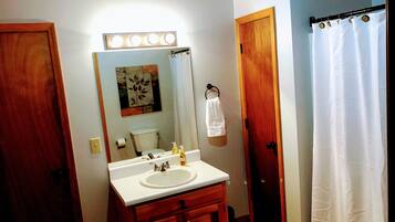 A bathroom with a wooden vanity, a sink, a mirror, a toilet, and a shower curtain.