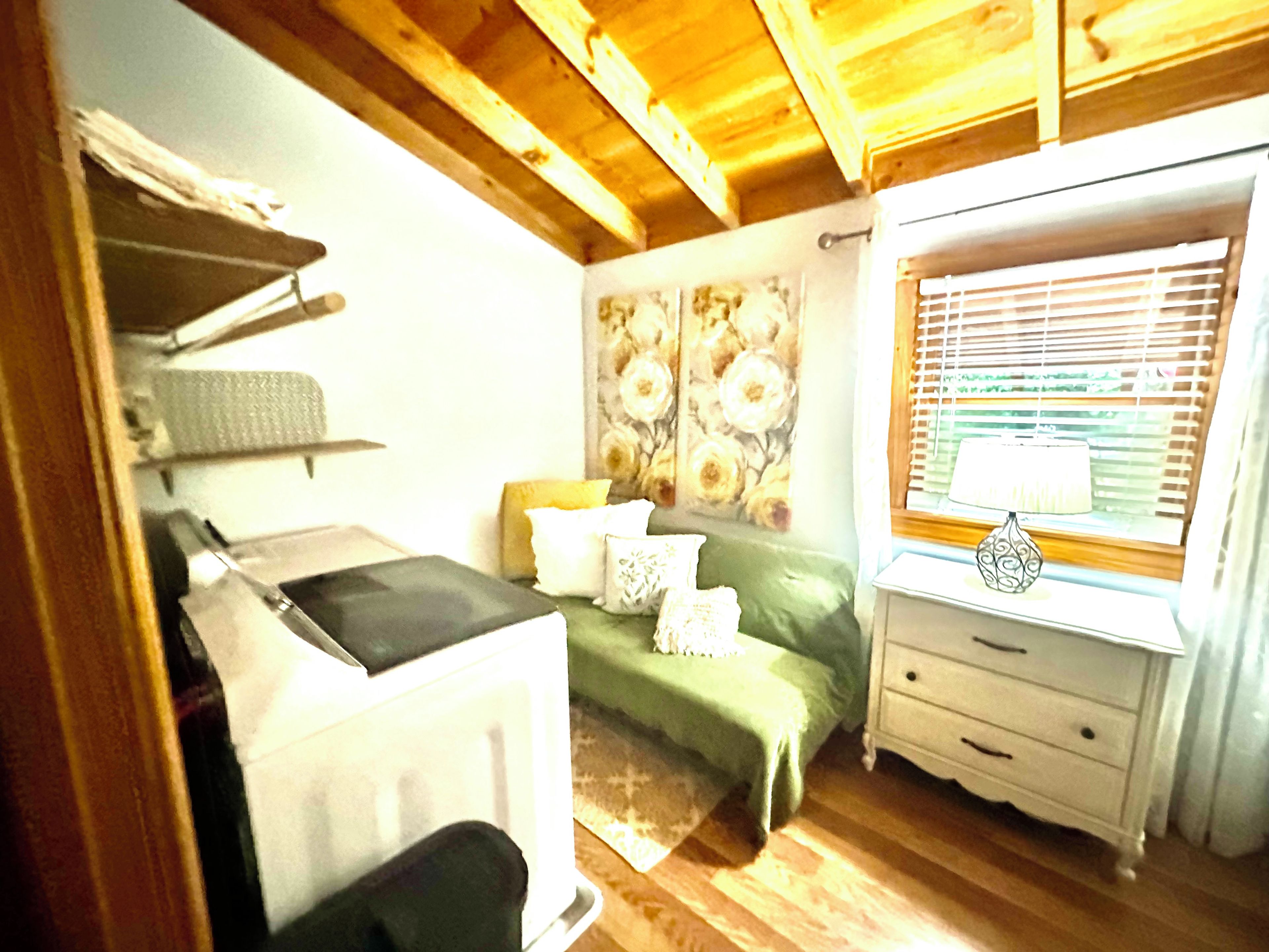 Un dormitorio con cama, mesita de noche, ventana con persianas y pared con papel tapiz floral.