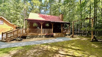 A wooden cabin with a porch and a swing set in a forested area.